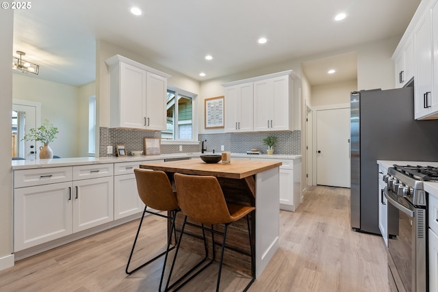 kitchen featuring light hardwood / wood-style floors, wooden counters, stainless steel range with gas stovetop, a kitchen breakfast bar, and white cabinets