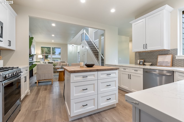 kitchen featuring backsplash, light hardwood / wood-style floors, butcher block countertops, white cabinetry, and appliances with stainless steel finishes