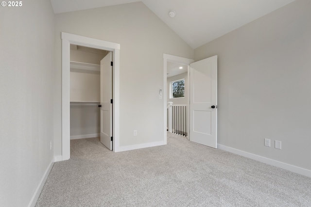 unfurnished bedroom featuring light carpet, a closet, a walk in closet, and lofted ceiling