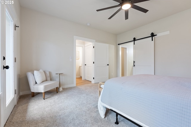 bedroom with ceiling fan, a barn door, light colored carpet, and connected bathroom