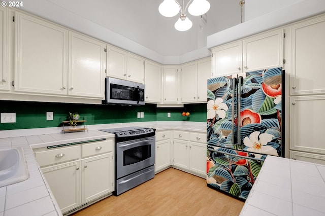 kitchen with tile countertops, light hardwood / wood-style floors, white cabinets, and stainless steel appliances