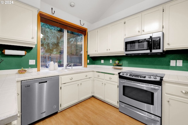 kitchen with white cabinetry, sink, tile countertops, appliances with stainless steel finishes, and light wood-type flooring