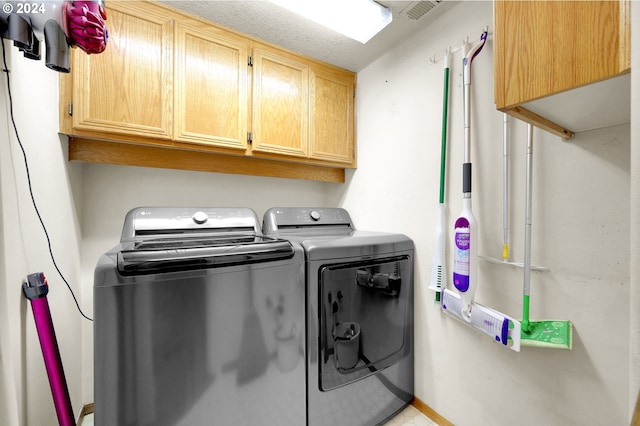 clothes washing area featuring cabinets, a textured ceiling, and washing machine and clothes dryer