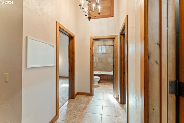 hall with light tile patterned floors, baseboards, and a notable chandelier