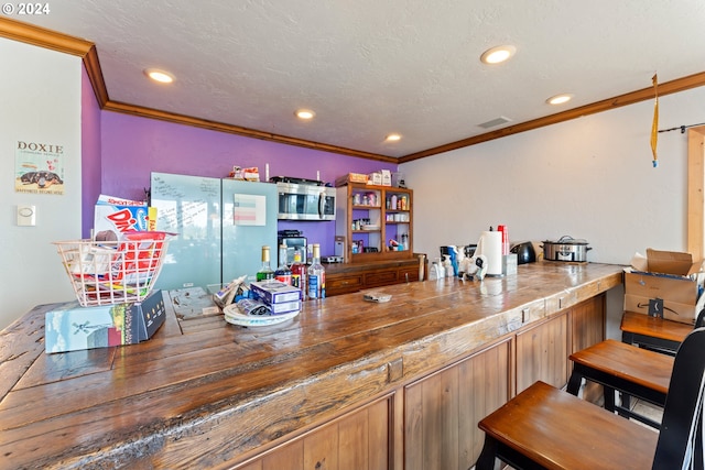 bar with a textured ceiling, a dry bar, stainless steel microwave, and crown molding