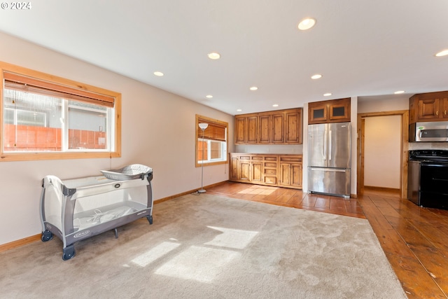 kitchen featuring baseboards, light colored carpet, brown cabinets, stainless steel appliances, and recessed lighting