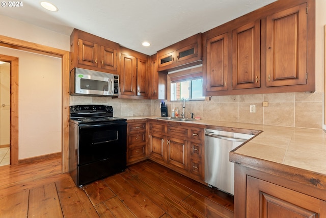 kitchen featuring dark wood-style floors, appliances with stainless steel finishes, brown cabinets, light countertops, and a sink