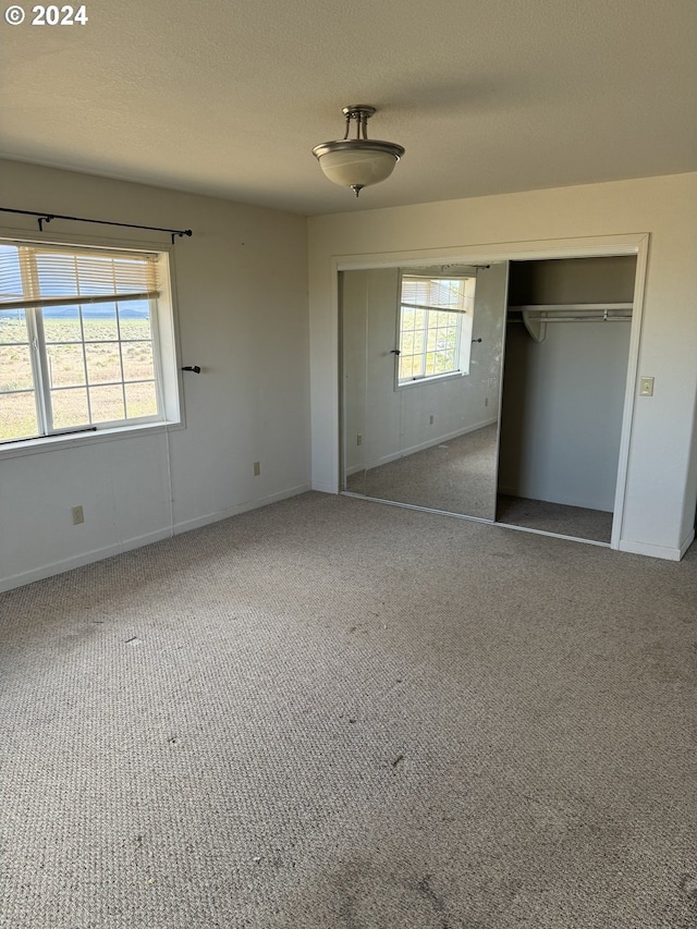 unfurnished bedroom with carpet floors, multiple windows, and a closet