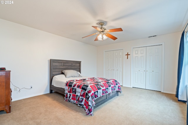 bedroom with ceiling fan, light carpet, and two closets