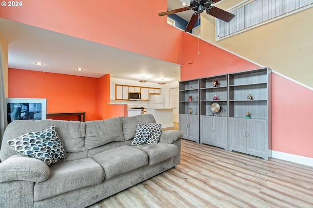 living room with ceiling fan, a towering ceiling, and light hardwood / wood-style floors