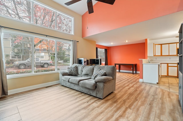 living room with ceiling fan, light hardwood / wood-style flooring, a towering ceiling, and sink