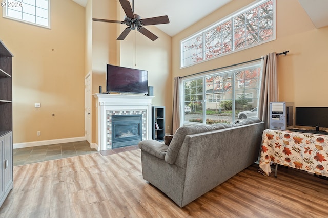 living room featuring a tile fireplace, a high ceiling, ceiling fan, and wood-type flooring