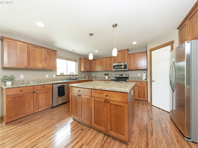 kitchen with appliances with stainless steel finishes, sink, hanging light fixtures, and light wood-type flooring