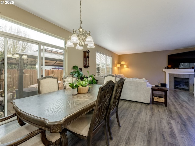 dining space with wood-type flooring, a notable chandelier, and a tiled fireplace