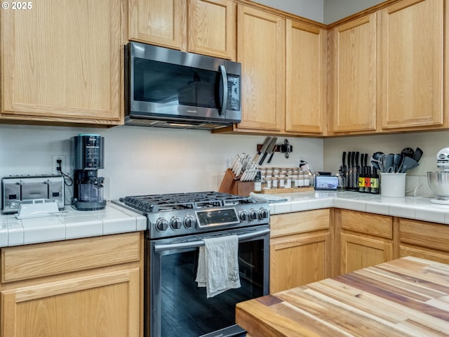 kitchen with appliances with stainless steel finishes, tile countertops, and light brown cabinets