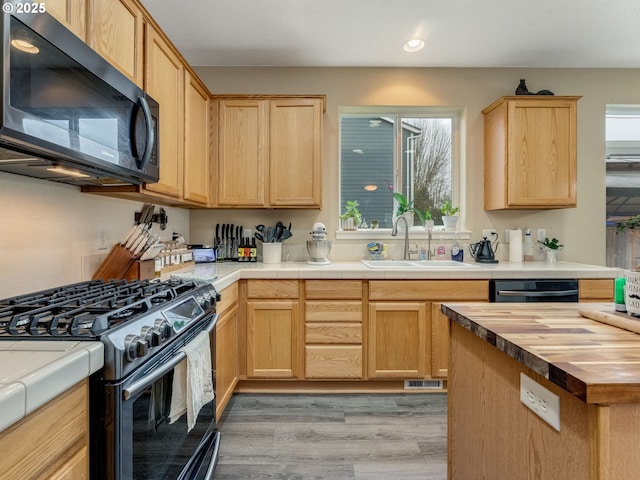 kitchen featuring gas stove, light brown cabinets, sink, tile countertops, and light wood-type flooring