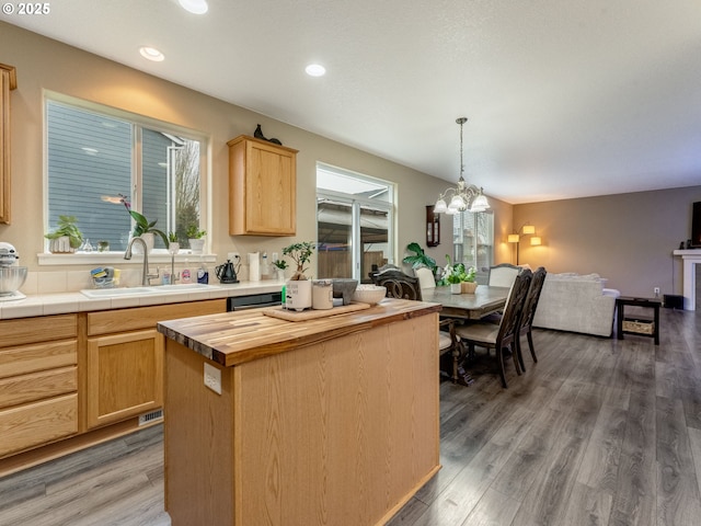 kitchen with a center island, hanging light fixtures, tile counters, light brown cabinetry, and dark hardwood / wood-style flooring