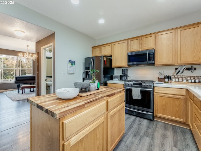 kitchen with appliances with stainless steel finishes, an inviting chandelier, hanging light fixtures, hardwood / wood-style flooring, and butcher block countertops