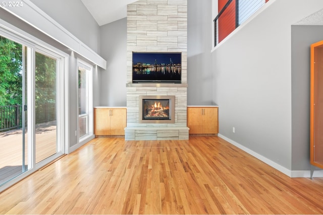 unfurnished living room featuring high vaulted ceiling, light wood-style flooring, baseboards, and a stone fireplace