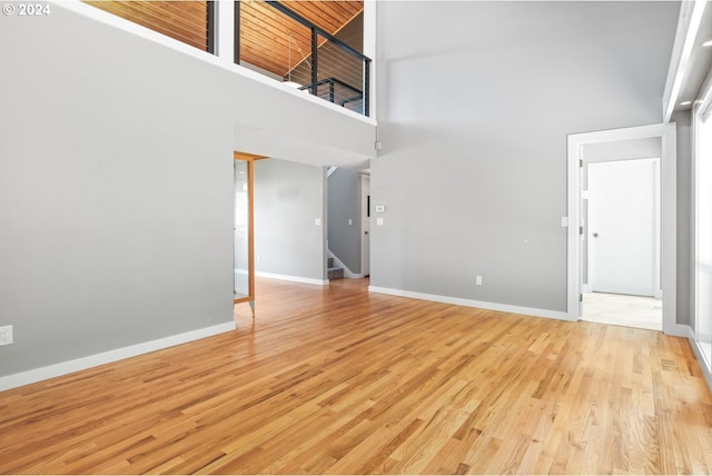 unfurnished living room featuring baseboards, a towering ceiling, light wood finished floors, and stairs