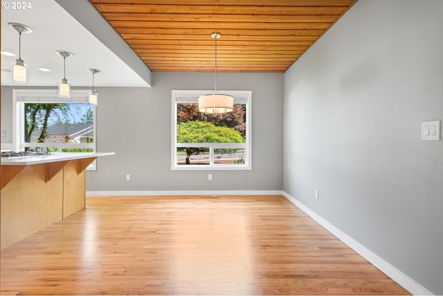 unfurnished dining area with light wood-style floors, wooden ceiling, and baseboards