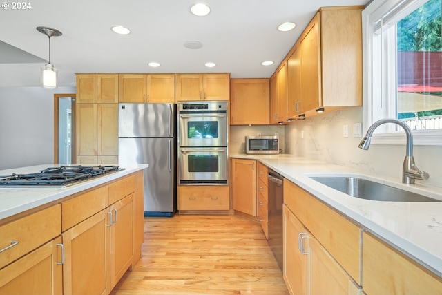 kitchen with recessed lighting, a sink, appliances with stainless steel finishes, light wood finished floors, and decorative light fixtures