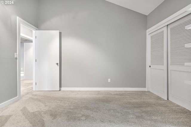 unfurnished bedroom with a closet, light carpet, vaulted ceiling, and baseboards