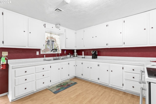 kitchen featuring visible vents, light wood-style flooring, a sink, light countertops, and white cabinets