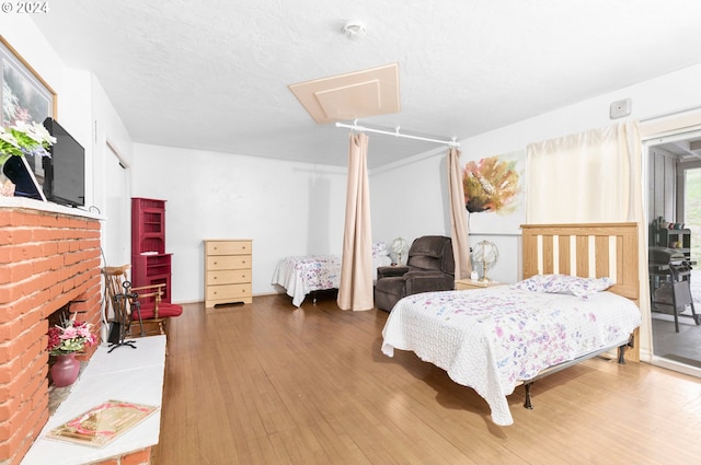 bedroom featuring a textured ceiling, attic access, wood finished floors, and a fireplace