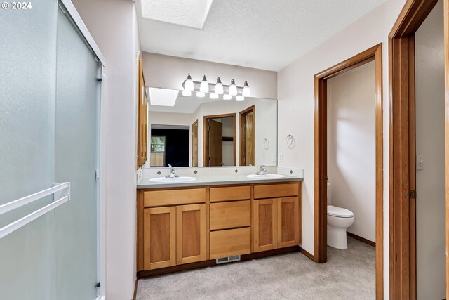 bathroom with toilet, vanity, a skylight, a textured ceiling, and an enclosed shower