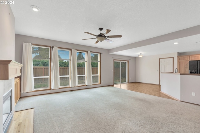 unfurnished living room with light hardwood / wood-style flooring, a textured ceiling, and ceiling fan