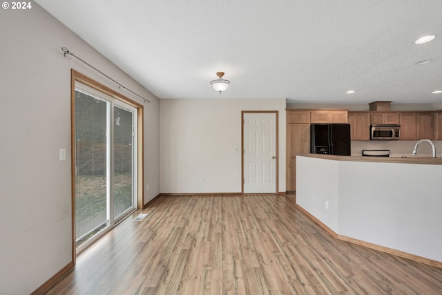 unfurnished living room with sink, a textured ceiling, and light hardwood / wood-style floors