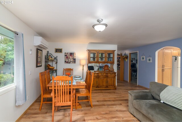 dining room with a wall mounted air conditioner, a wealth of natural light, and light hardwood / wood-style floors