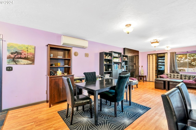 dining room with a textured ceiling, light wood-type flooring, and a wall unit AC