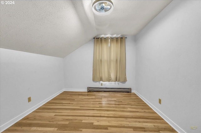 additional living space featuring a baseboard radiator, vaulted ceiling, a textured ceiling, wood finished floors, and baseboards