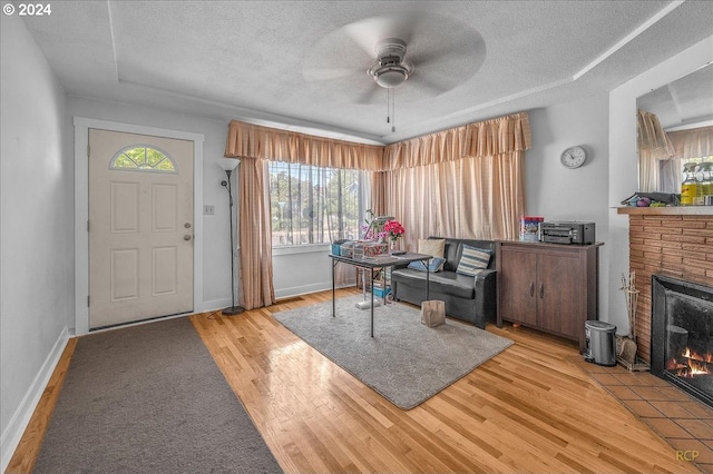 entryway with ceiling fan, a fireplace, a textured ceiling, and light hardwood / wood-style flooring