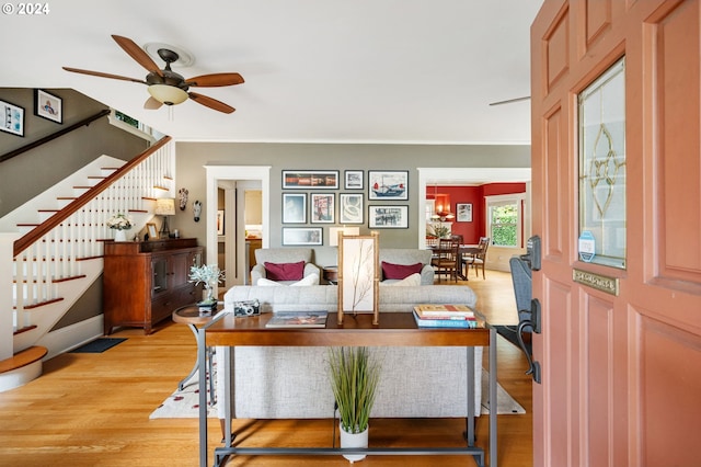 living area featuring light wood-type flooring, a ceiling fan, and stairs