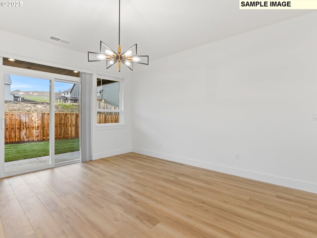 spare room featuring light wood-type flooring, a notable chandelier, visible vents, and baseboards