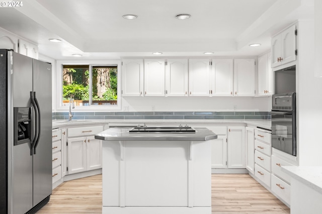 kitchen featuring white cabinets, black appliances, a center island, sink, and a tray ceiling