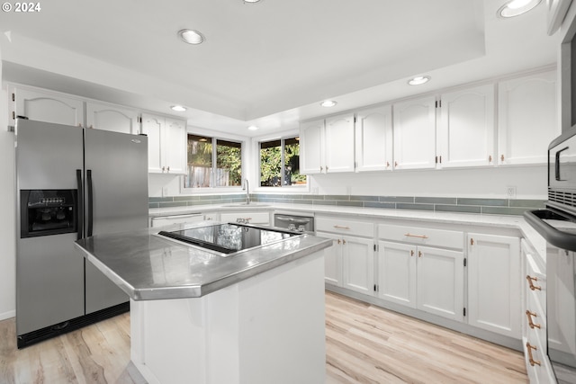 kitchen with a kitchen island, a raised ceiling, white cabinets, and stainless steel fridge