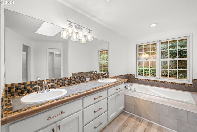 bathroom with wood-type flooring, vanity, a skylight, decorative backsplash, and a relaxing tiled tub