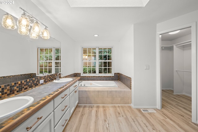 bathroom featuring tasteful backsplash, vanity, a relaxing tiled tub, and hardwood / wood-style flooring