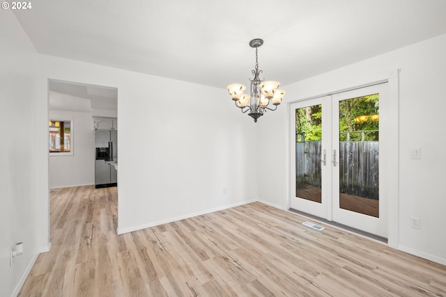 empty room featuring french doors, a wealth of natural light, an inviting chandelier, and light hardwood / wood-style floors