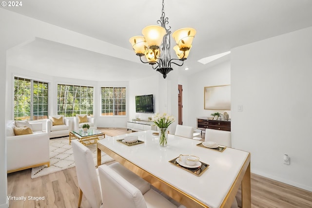 dining space with light hardwood / wood-style floors, vaulted ceiling, and an inviting chandelier