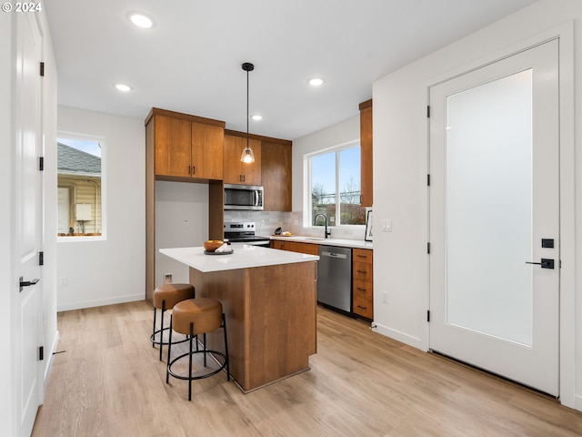 kitchen with appliances with stainless steel finishes, light wood-type flooring, sink, decorative light fixtures, and a center island