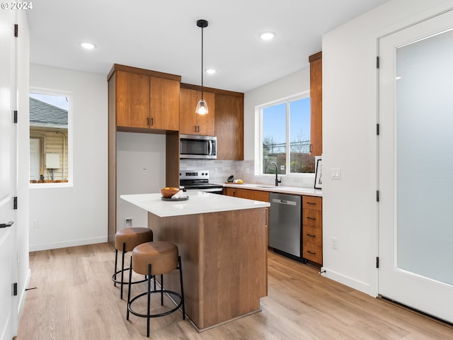 kitchen featuring sink, stainless steel appliances, backsplash, light hardwood / wood-style floors, and decorative light fixtures