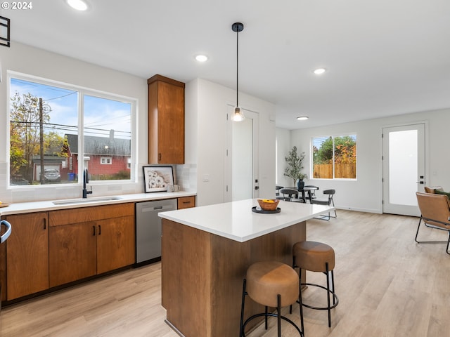 kitchen featuring tasteful backsplash, dishwasher, sink, hanging light fixtures, and light wood-type flooring