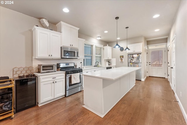 kitchen with decorative light fixtures, appliances with stainless steel finishes, beverage cooler, and white cabinetry