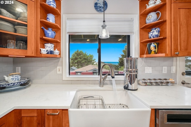 kitchen featuring sink, decorative backsplash, light stone countertops, and pendant lighting