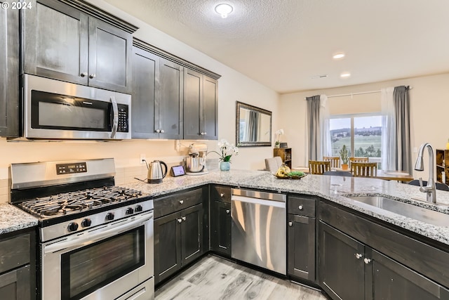 kitchen featuring appliances with stainless steel finishes, sink, light stone countertops, a textured ceiling, and light hardwood / wood-style flooring